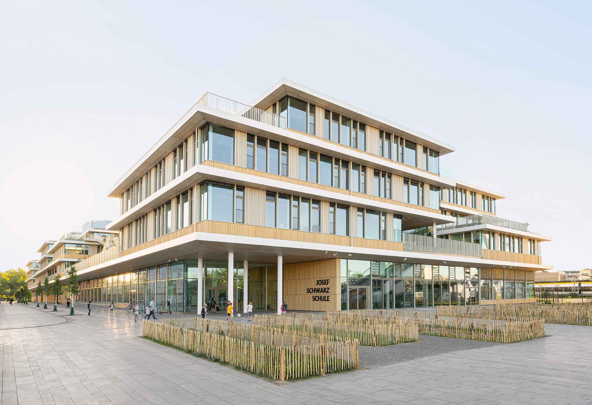 Außenansicht über Eck des Holz-Hybrid-Baus Josef-Schwarz-Schule in Heilbronn mit eingezäunten Rasenflächen im Vordergrund.