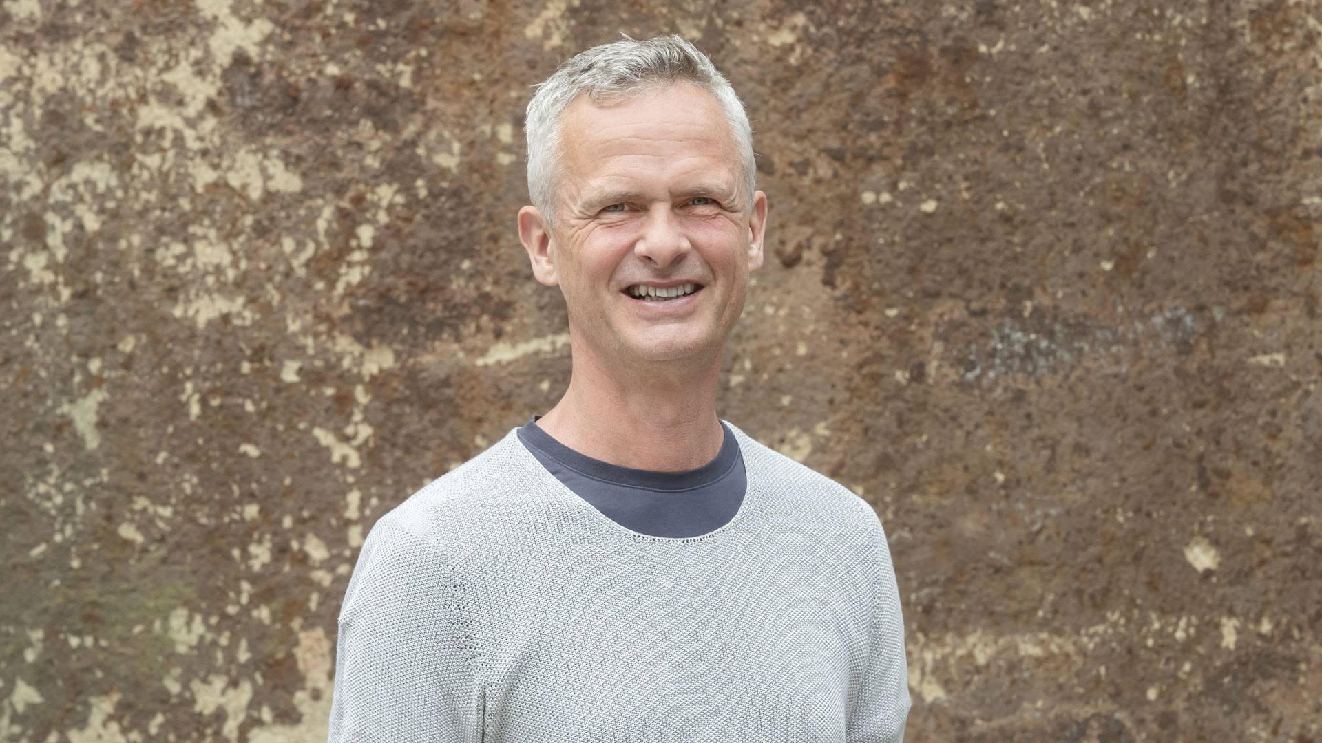 Das Foto zeigt ein Portrait von Peter Bachmann vor einer braunen Wand. 