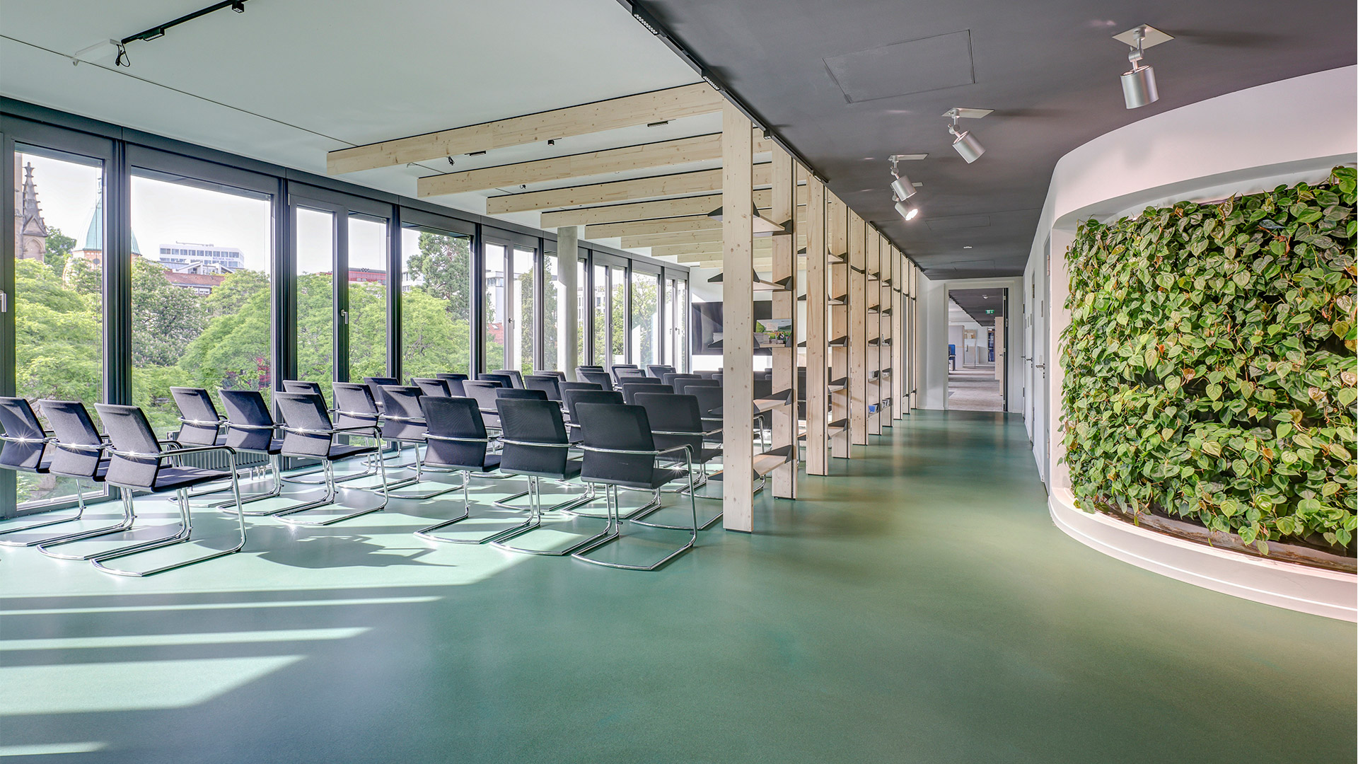 Offener Veranstaltungsbereich (Forum) mit Foyer, begrünter Wand, Fensterfront, Reihenbestuhlung.