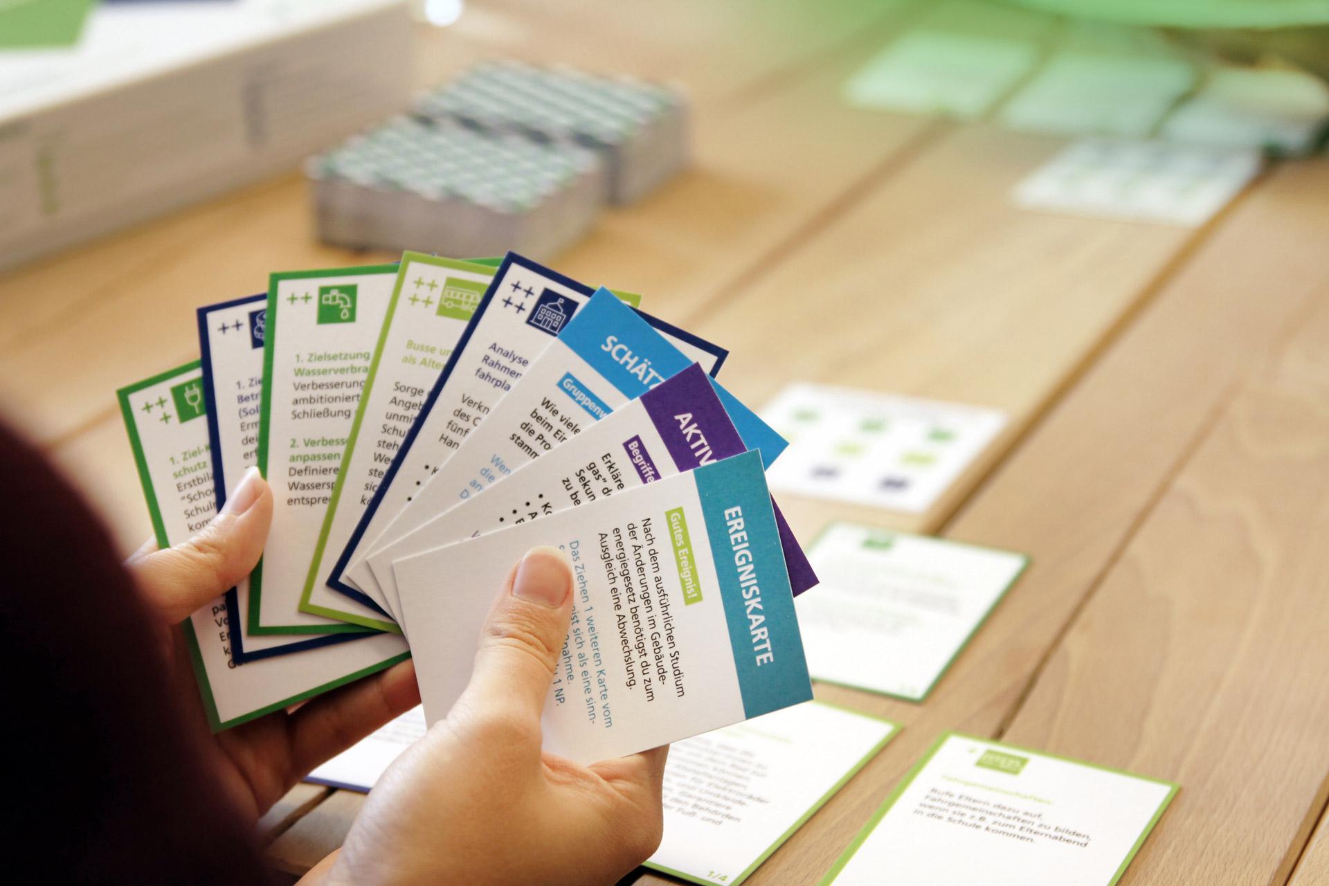 Zwei Personen spielen das DGNB Kartenspiel. Der Fokus ist auf die Handkarten von der Person im Vordergrund gerichtet. 