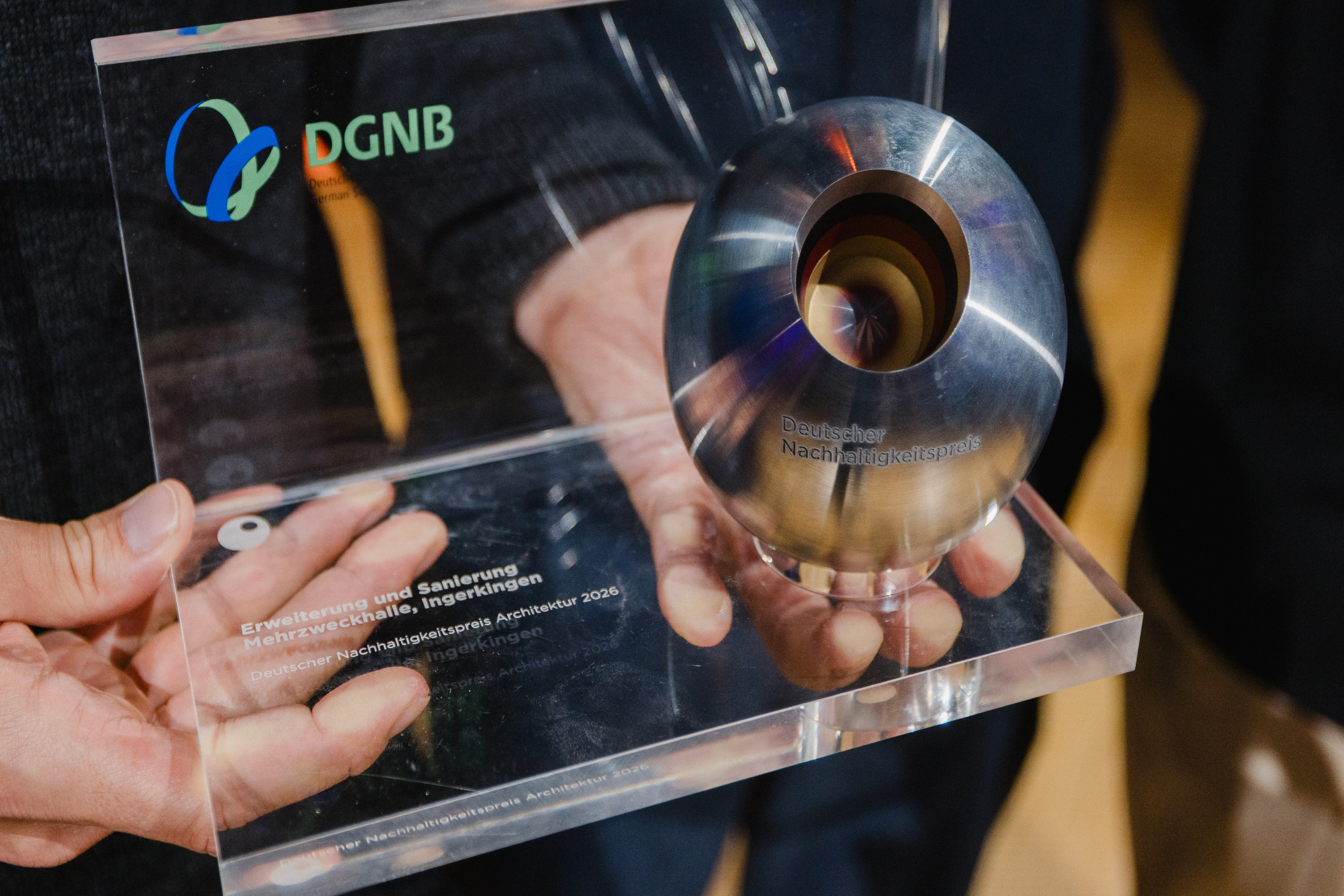 Zwei Hände halten die Preiskugel vom Deutschen Nachhaltigkeitspreis Architektur.