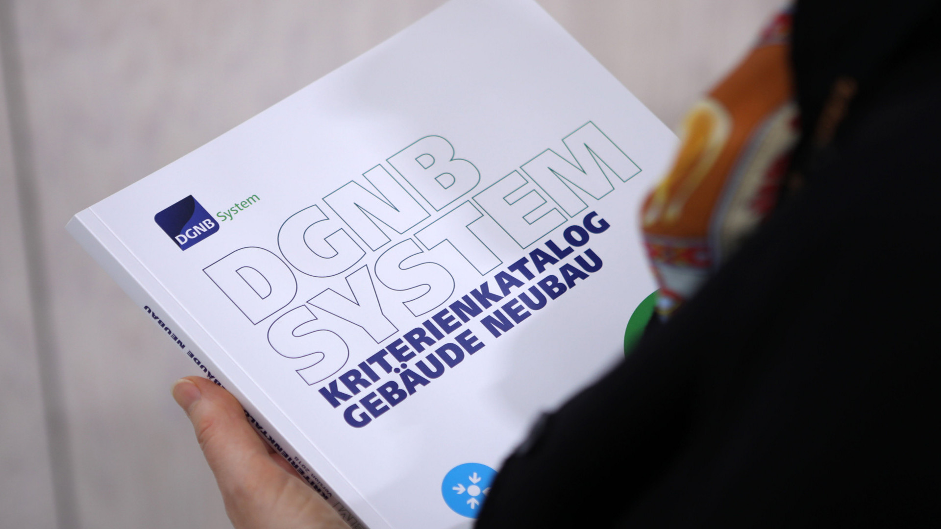 Foto von einer Person, die den DGNB Kriterienkatalog Gebäude Neubau in der Hand hält