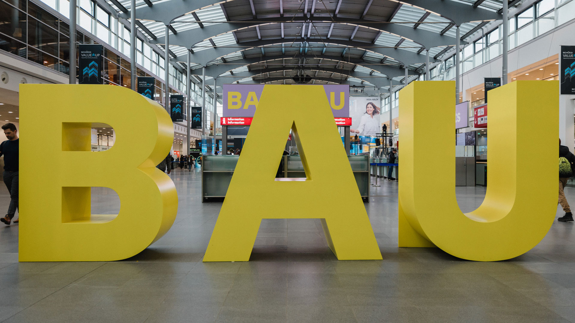 Das Foto zeigt drei große gelbe Buchstaben: BAU. Sie sind in der Eingangshalle der Messe München fotografiert.