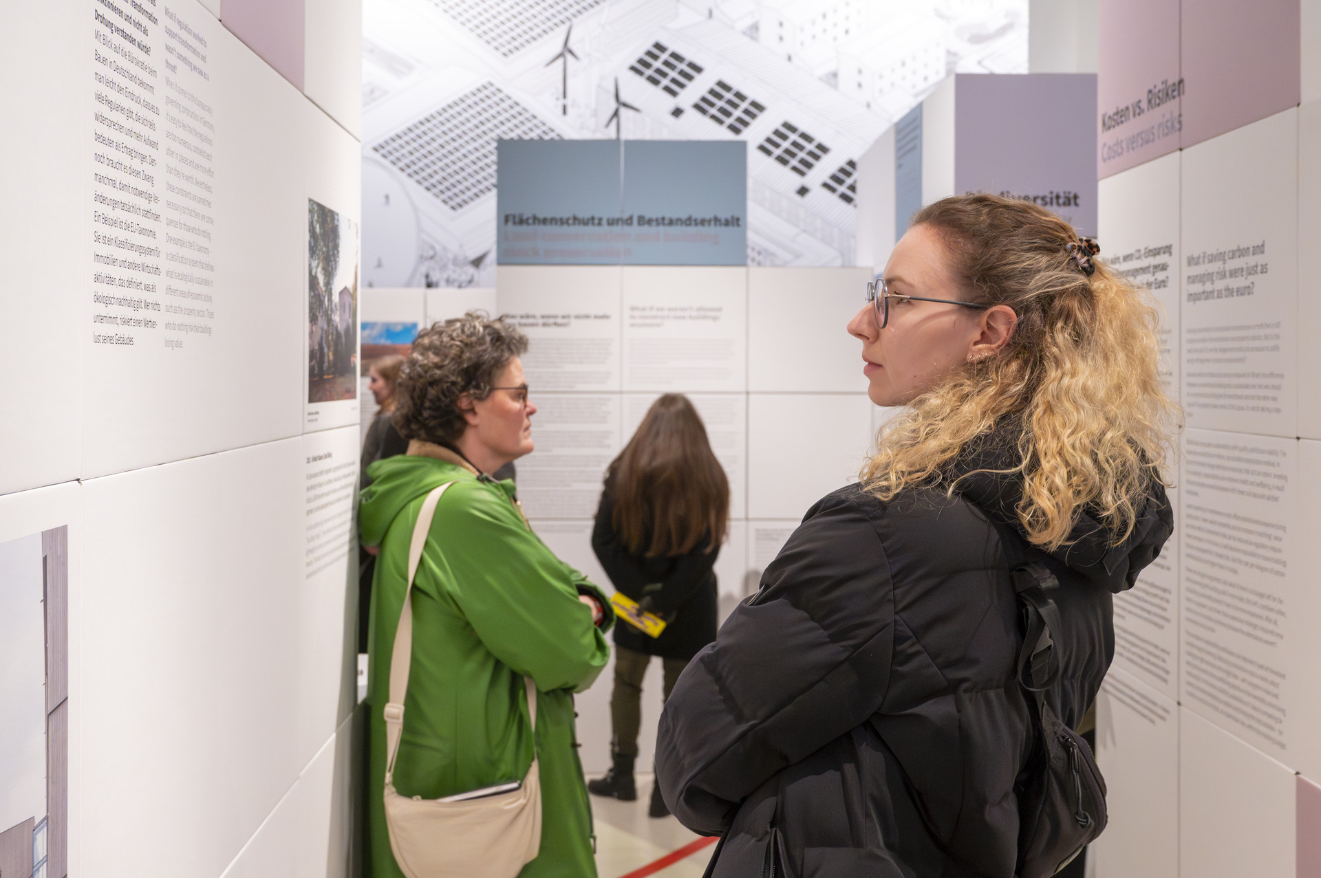 Impression von der Eröffnung der DGNB Ausstellung bei Aedes. Menschen sind zwischen den aus Pappwürfeln aufgebauten Ausstellungswänden zu sehen, wie sie die Inhalte lesen.