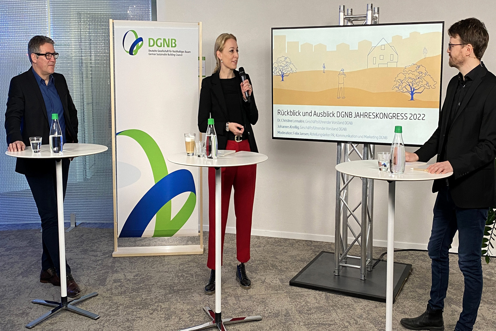 Gesprächsrunde beim DGNB Jahreskongress 2022 mit Johannes Kreißig, Dr. Christine Lemaitre und Felix Jansen - jeweils an einem Stehtisch stehend -  vor einem großen Bildschirm.