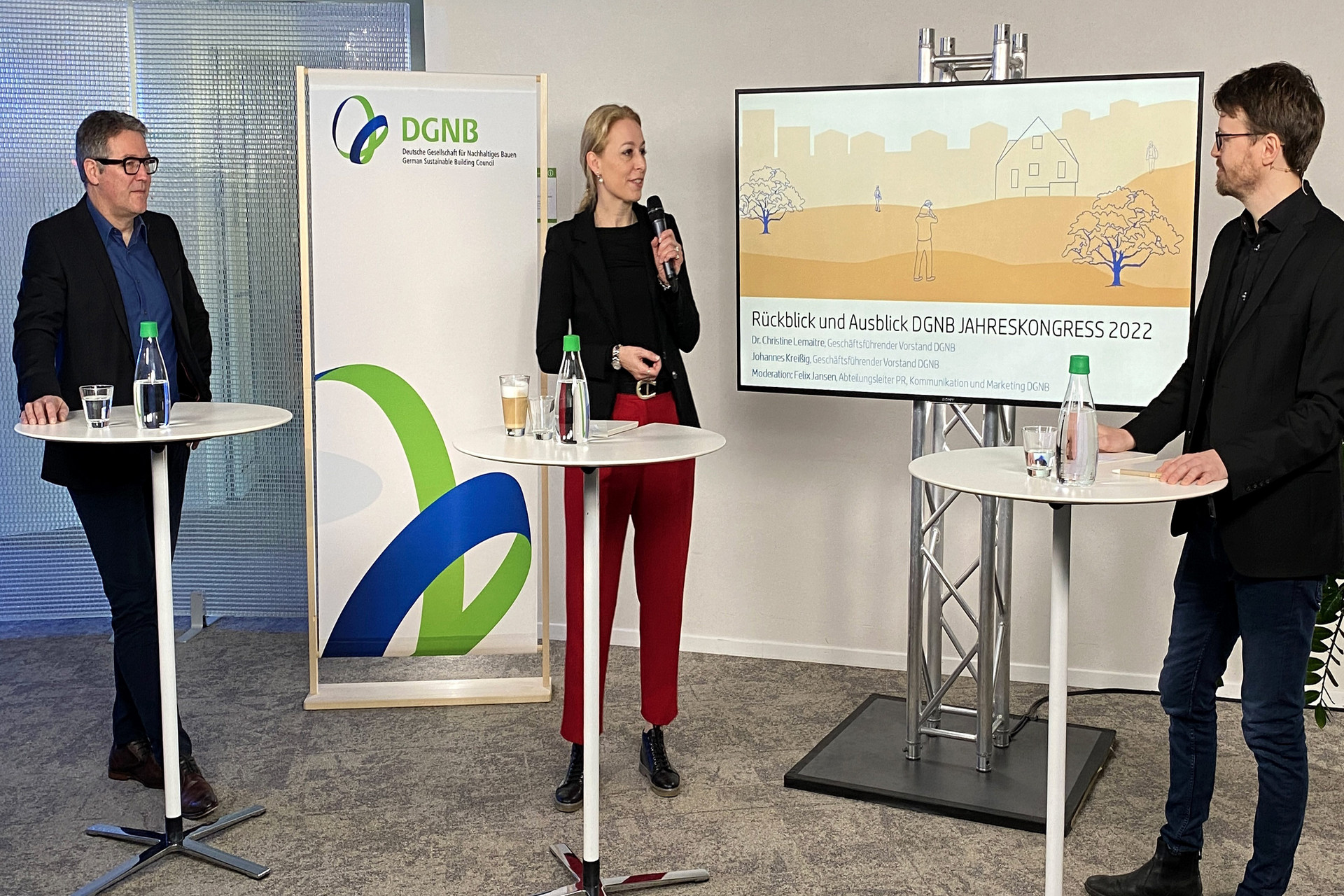 Gesprächsrunde beim DGNB Jahreskongress 2022 mit Johannes Kreißig, Dr. Christine Lemaitre und Felix Jansen - jeweils an einem Stehtisch stehend -  vor einem großen Bildschirm.