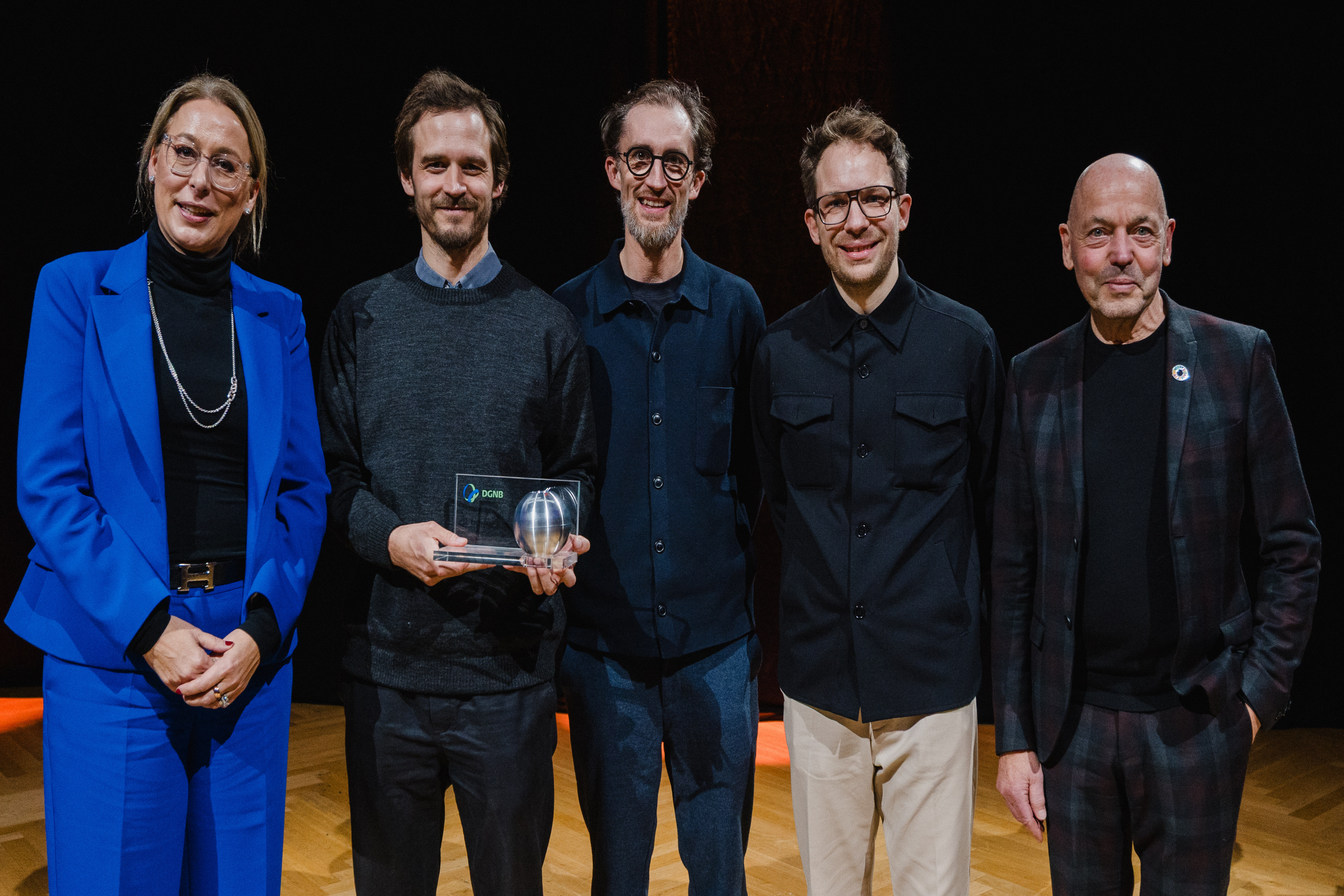 Gruppenbild der Gewinner des 13. Deutschen Nachhaltigkeitspreises Architektur mit Geschäftsführendem Vorstand der DGNB, Dr. Christine Lemaitre links im Bild und DGNB Präsident Amandus Samsøe Sattler rechts im Bild..