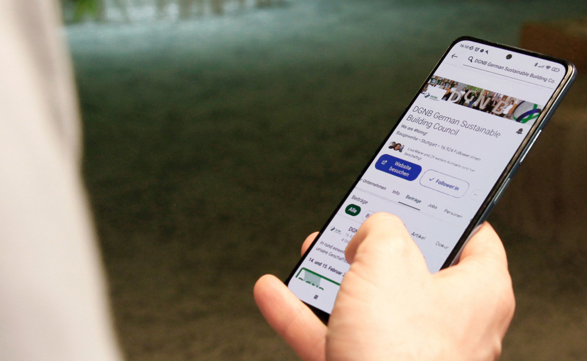 Person mit Smartphone in der Hand. Auf dem Handy ist der LinkedIn Account der DGNB zu sehen.