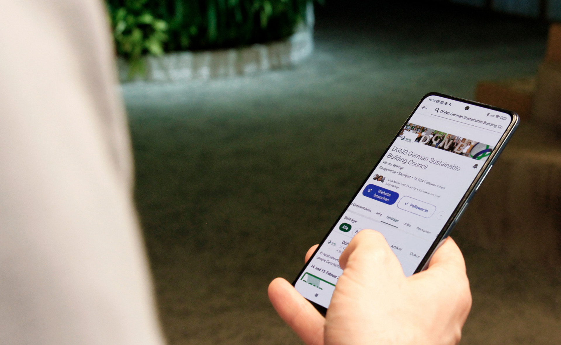 Person mit Smartphone in der Hand. Auf dem Handy ist der LinkedIn Account der DGNB zu sehen.