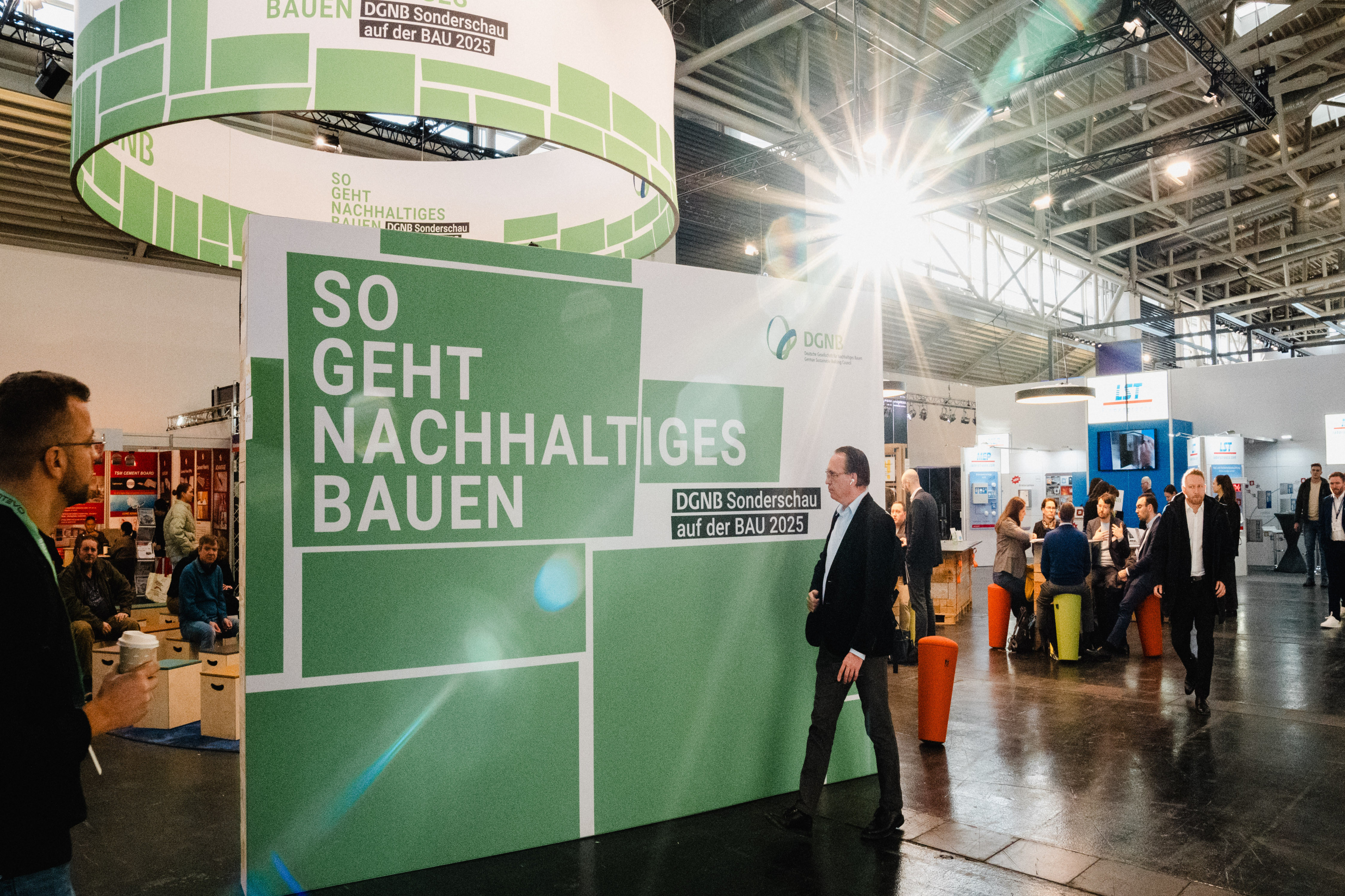 DGNB Pressebild Aufnahme des DGNB messestandes zur BAU 2025 mit grün-motivig bedruckter Wand mit dem Motto "So geht nachhaltiges Bauen".