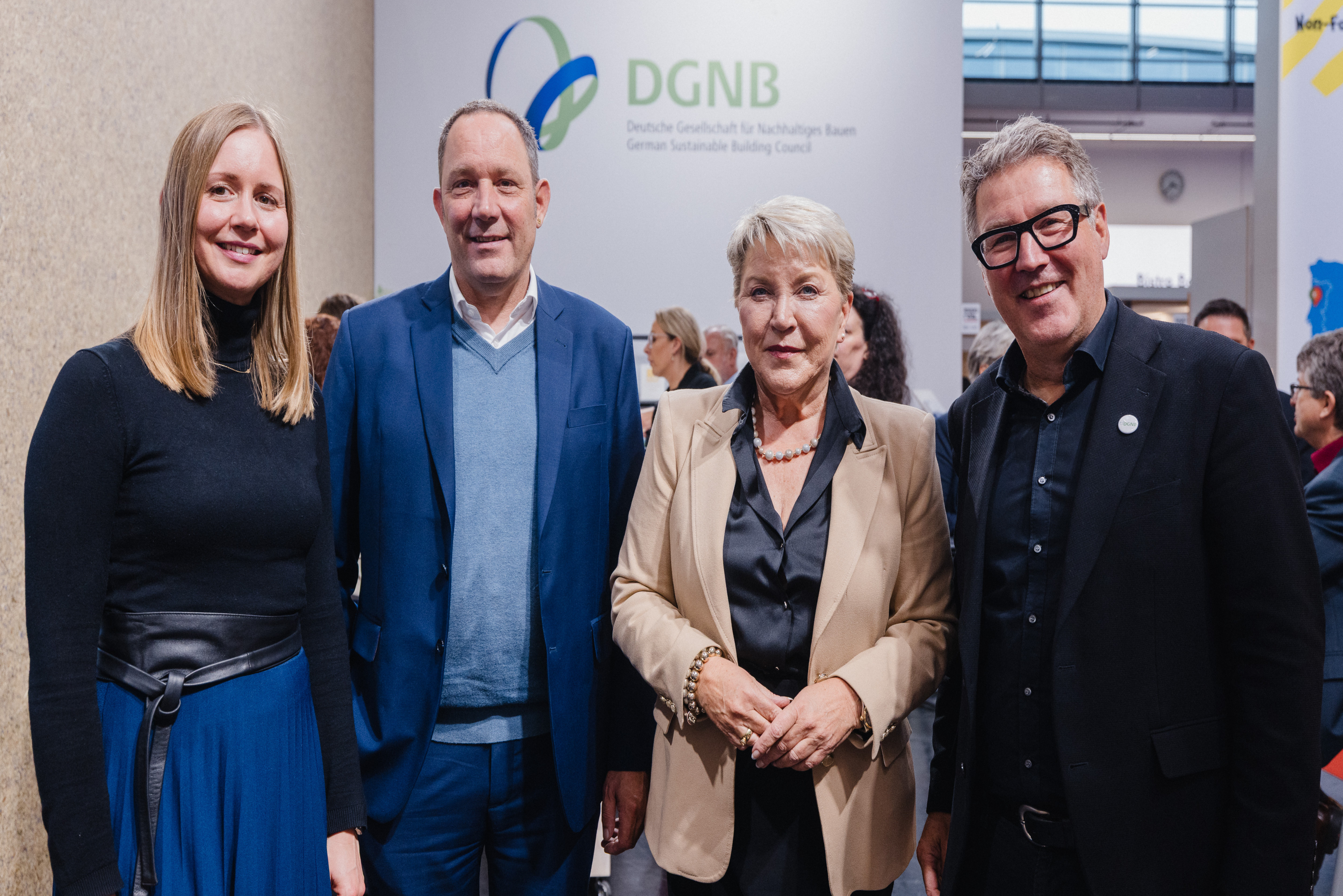 Gruppenbild mit vier Personen vor einem Element des DGNB Stands auf der Expo Real 2025 mit DGNB Vereinslogo.